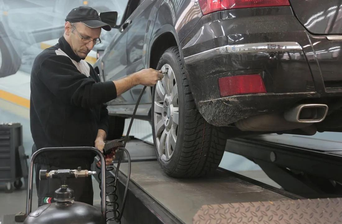 A technician checking a vehicle's tire pressure with an air gauge